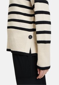 Strickpullover mit schwarzen und cremefarbenen Streifen, Rundhalsausschnitt, strukturierter Stoff, schwarze Knopfdetails und SC SY-Logo an der unteren Seite.