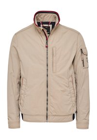 Beige lightweight jacket with a high collar, front zipper, side pockets, and a decorative left sleeve pocket. Red and navy accents visible.