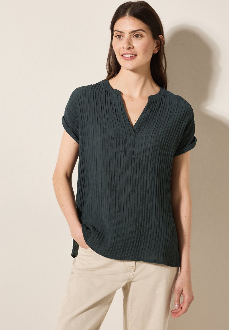 Mørkegrøn, tekstureret bluse med korte, rullede ærmer og V-udskæring. Stoffet har lodrette plisseringer for et afslappet design.