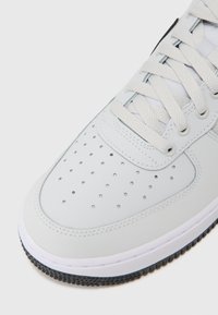 Light gray sneaker with a smooth leather upper, perforated toe box, flat laces, cushioned tongue, and white rubber sole with textured grip.