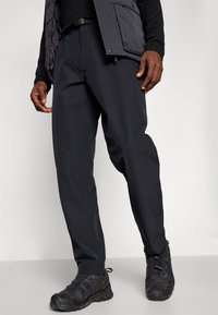 Black lightweight pants with a relaxed fit, featuring a smooth texture and side pockets, paired with black athletic shoes.