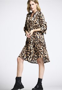 Leopardenmusterkleid mit V-Ausschnitt und langen Ärmeln, ausgestattet mit einem gestuften Rock und leichtem, fließendem Stoff. Kombiniert mit schwarzen Schnürstiefeln.