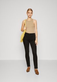 Top sin mangas beige, jeans ajustados negros y botas de tacón marrones; acentuado con un bolso de punto amarillo; textura suave en toda la prenda.