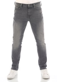 Jeans de mezclilla gris con corte slim, ligero desvanecimiento, diseño de cinco bolsillos y costuras en contraste. Combinados con zapatillas blancas.