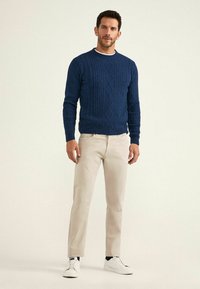Pull en maille côtelée marine avec motif en losanges, col rond, porté avec un pantalon beige et des baskets blanches. Texture douce, design ajusté.