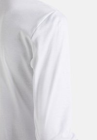 Camicia bianca a maniche lunghe realizzata in un tessuto leggero e morbido, con scollatura a girocollo e maniche dritte. Senza motivi o dettagli visibili.