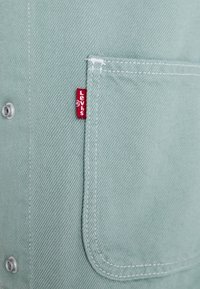 Miętowozielony denim ma kieszeń z czerwoną metką Levi's, srebrne guziki oraz widoczne detale przeszyć.