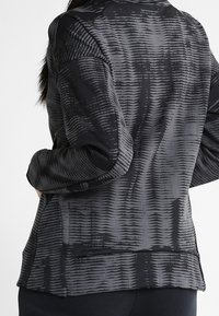 Veste à motifs noirs et gris avec une surface texturée, un design structuré, une coupe slim et un col avec un détail de poche arrière.