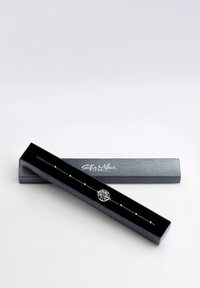 Silverarmband med en träddesign, prytt med små runda pärlor på ett delikat kedja, presenterat i en svart smyckeslåda.