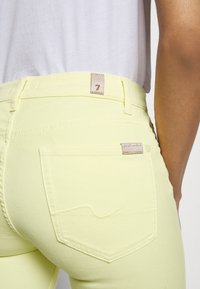 Jeans amarillos de talle alto con un acabado texturizado, que cuentan con bolsillos traseros y una etiqueta de marca en la cinturilla. Fabricados en tejido suave y con un diseño ajustado.