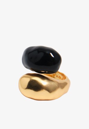 Hladké, nepravidelného tvaru zlaté a čierne prstene naskladané na seba s lesklým, lešteným povrchom na bielom pozadí.