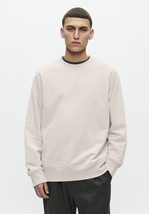 Helles rosa Sweatshirt mit Raglanärmeln, rundem Ausschnitt und gerippten Bündchen. Die Kombination mit dunklen Hosen vervollständigt den Look.