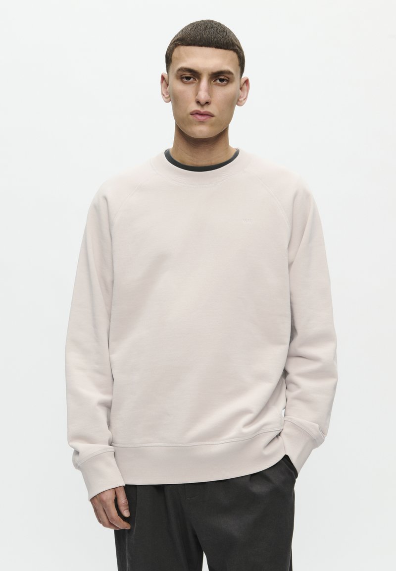 Helles rosa Sweatshirt mit Raglanärmeln, rundem Ausschnitt und gerippten Bündchen. Die Kombination mit dunklen Hosen vervollständigt den Look.