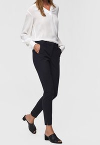Biała, lekka bluzka z długim rękawem i dekoltem w serek. Granatowe, dopasowane spodnie ankle z bocznymi kieszeniami, połączone z czarnymi klapkami na gołych stopach.
