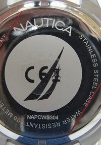 Rozsdamentes acél óra hátlapján a "Nautica" felirat, CE jelölés és vízálló specifikációk találhatóak. Fekete háttér ezüst kiegészítőkkel és gravírozott részletekkel.