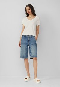 T-shirt blanc à col en V associé à un short en denim bleu clair, avec une coupe droite, un ourlet effiloché et des sandales blanches décontractées.