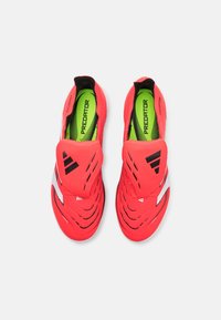 Red soccer shoes with a sleek design, made of synthetic material, featuring a textured surface, slip-on style, and a green insole.