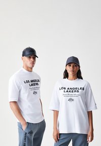 Bijele majice s crnim natpisom "Los Angeles Lakers", sivi dukserice s logotipom i odgovarajuće sive kape. Opusti kroj, pamuk.