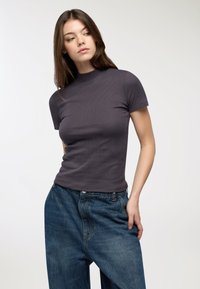 Ciemnoszara, prążkowana bluzka z krótkim rękawem i wysokim kołnierzem, zestawiona z luźnymi, niebieskimi dżinsami. Proste, czyste linie i swobodny fason.