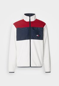 Giacca in pile con pannelli superiori rossi e inferiori navy, corpo bianco, collo alto, zip frontale e tasca sul petto con dettaglio del logo.