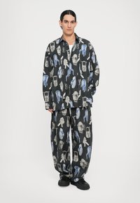Chemise et pantalon assortis à motifs noirs illustrant des ustensiles et des chaises en bleu et gris. Design ample, style décontracté.