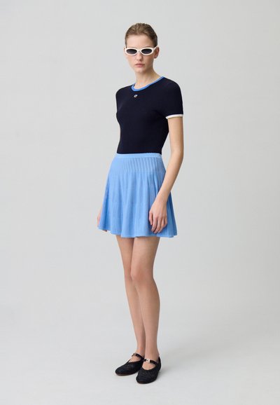 Top de rayas marino con acentos en azul claro combinado con una falda plisada azul claro. Zapatos negros trenzados, accesorios mínimos, gafas de sol elegantes.