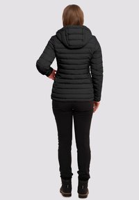 Zwarte pufferjack met een horizontaal gestikt ontwerp, een capuchon en lange mouwen. Draagt het met zwarte broek en laarzen, gezien van achteren.