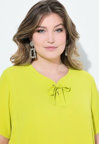 Top verde lime con maniche corte, scollatura a V e un fiocco decorativo. Presenta un tessuto morbido e una vestibilità rilassata.