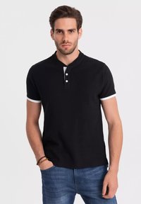 Černé polo tričko s krátkým rukávem, s knoflíkovou légou a bílými akcenty na límci a rukávech, vyrobené z měkké, texturované tkaniny.