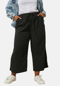 Svarta beskurna byxor med en texturerad finish, elastisk midja och dragsko. Kombinerat med en vit T-shirt och vita sneakers.