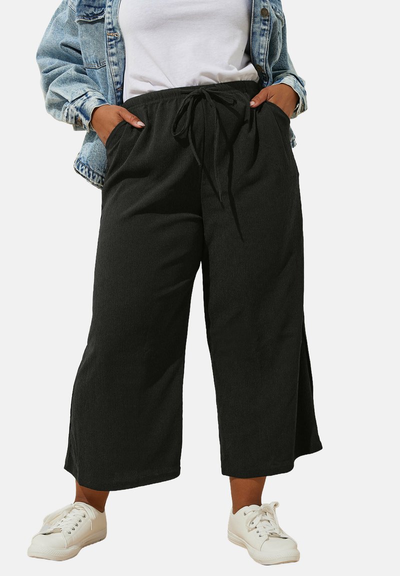 Svarta beskurna byxor med en texturerad finish, elastisk midja och dragsko. Kombinerat med en vit T-shirt och vita sneakers.