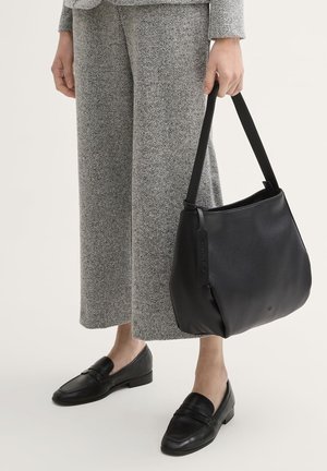 Schwarze Leder-Shopper-Tasche mit einer weichen, strukturierten Oberfläche und einem einzelnen schwarzen Riemen. Trägt man zu grauen Hahnentritthosen und schwarzen Loafers.