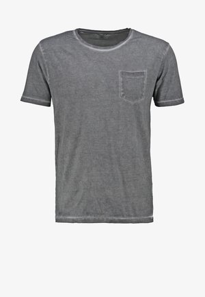 T-shirt en coton gris avec une poche poitrine, assorti à un short en denim bleu clair retroussé et des baskets rouges. Sac à dos noir porté sur une épaule.