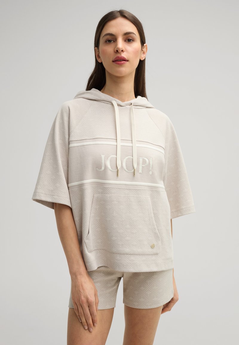 Beige hoodie met korte mouwen, voorzien van "JOOP!" in lichte borduursel en een voorzak. Bijpassende shorts met een subtiel patroon.