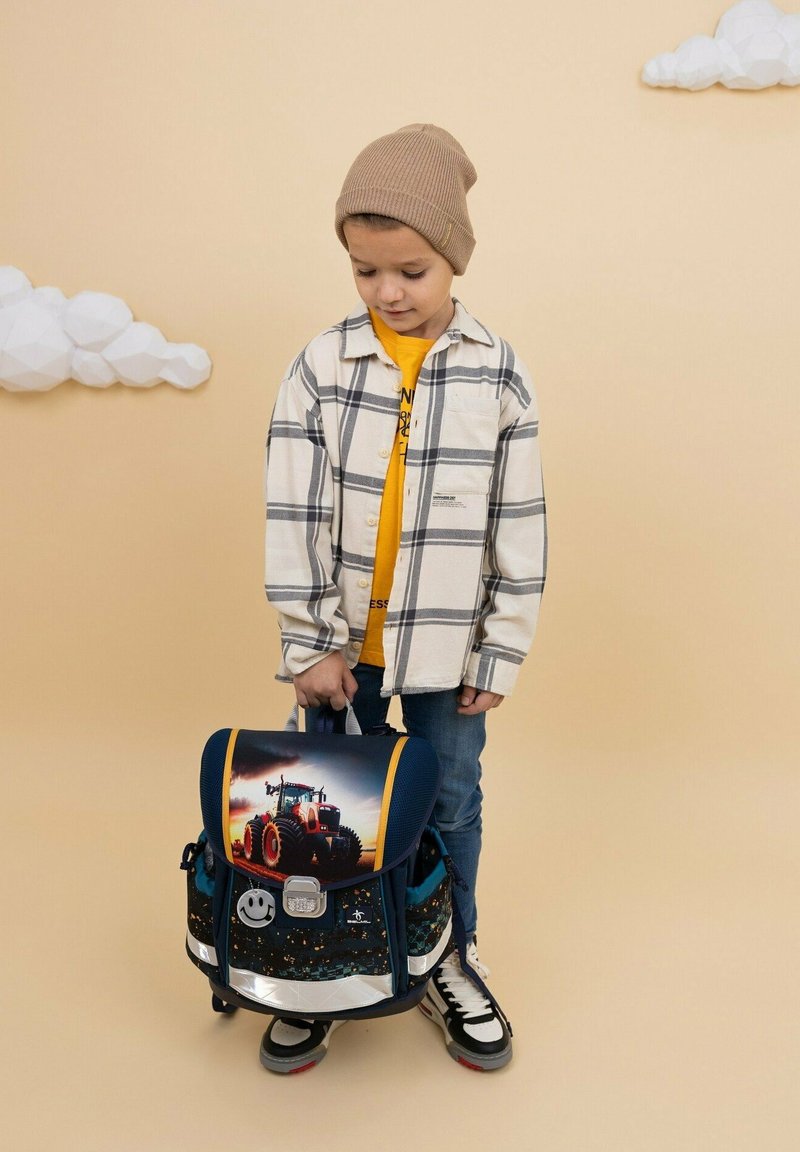 Rucksack mit einem Traktor-Design auf dem Deckel, dunkelblaum Körper, reflektierenden Akzenten und verstellbarem Gurt; aus strapazierfähigem Stoff gefertigt.