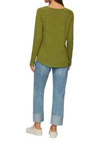 Langärmliges olivgrünes Oberteil mit rundem Ausschnitt, kombiniert mit hellblauen Jeans aus Denim mit aufgerollten Säumen. Weiße Sneakers runden das Outfit ab.