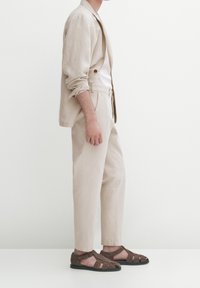 Ljus beige linneskjorta, vit skjorta och matchande beige byxor. Bruna mockasandaler med snörning och svarta sulor.