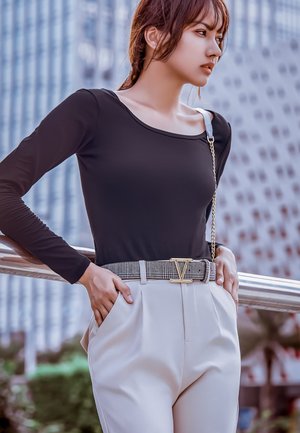 Zwarte lange mouwen top met een brede halslijn, gecombineerd met hoog opgesneden lichtbeige broek met een riem met zilveren accenten.