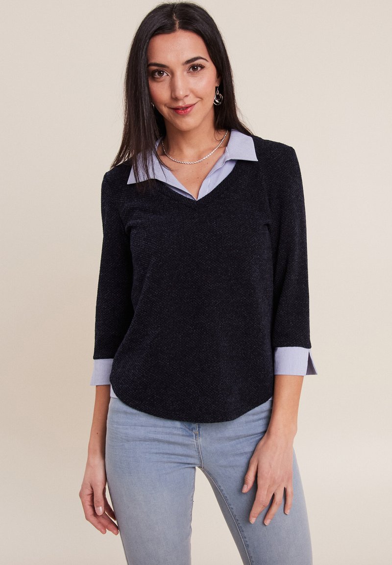 Haut noir à col en V avec des manches trois-quarts et des poignets à rayures bleu clair. Tissu texturé avec une finition lisse, associé à un denim bleu clair.
