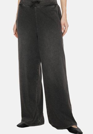 Schwarze Hosen mit weitem Bein und Kordelzug in der Taille, getragen von einer Person, die mit leicht auseinander stehenden Füßen steht und die Hände seitlich ruhen lässt.