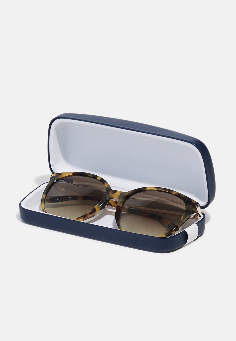 Occhiali da sole tartarugati con lenti marroni in una custodia rigida blu navy, con un interno liscio e un accento bianco sul lato.