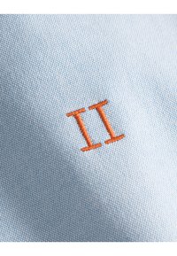 Light blue fabric features a textured weave, with an orange embroidered “II” prominently displayed in the center.