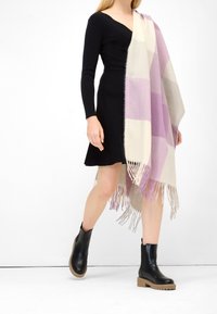 Sjalk i ullblandning med pastell-lila och krämfärgad rutmönster, fransade ändar, hängande över en figursydd svart klänning och kombinerad med svarta ankelboots.