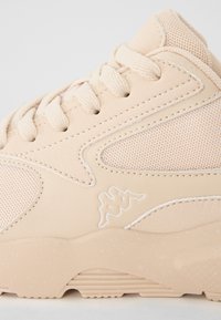 Világos bézs sneaker, amely hálós felsőrésszel, egybefüggő fűzőkkel, diszkrét velúr részletekkel és emelt gumitalppal rendelkezik, amely textúrázott mintázattal bír.