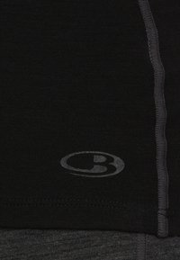 Schwarzes Sporttop aus glattem Stoff mit grauem Nähten. Verfügt über ein dezentes Logo nahe dem Saum und eine taillierte Passform.