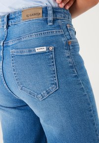 Los vaqueros de denim azul claro tienen una cintura alta, diseño de cinco bolsillos y una etiqueta de cuero en la parte posterior con el logo de la marca.