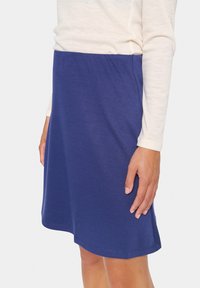 Jupe en coton bleu avec une texture lisse, de longueur genou, et une coupe droite simple, assortie à un haut à manches longues crème.