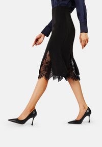 Gonna nera a matita con orlo in pizzo e spacchi laterali, abbinata a décolleté nere a punta. Texture liscia e silhouette elegante.