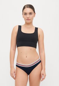 Haut de bain noir avec un décolleté carré et des bretelles larges, associé à un bas de bikini bleu marine avec une ceinture rayée rouge, blanche et bleue.