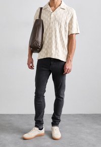 Vaaleanbeige lyhythihainen paita, jossa on teksturoidulla ruutukuvioinnilla, yhdistetty kapeisiin mustiin farkkuihin ja beigeihin tennareihin kumipohjalla. Ruskea nahkalaukku.